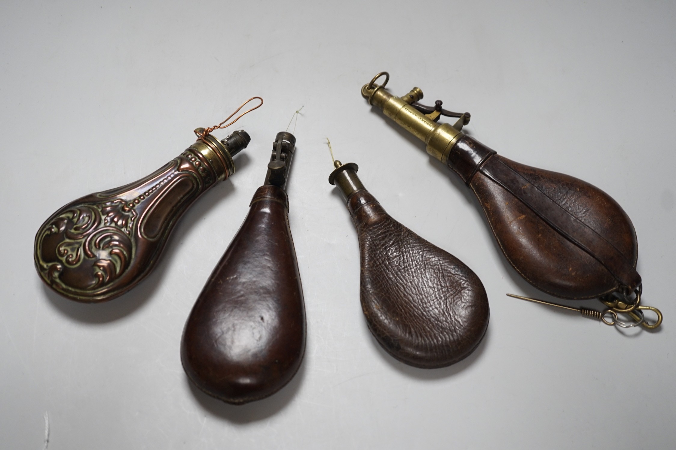 Four brass mounted powder flasks, to include three leather flasks, and one copper. Largest 24cm long